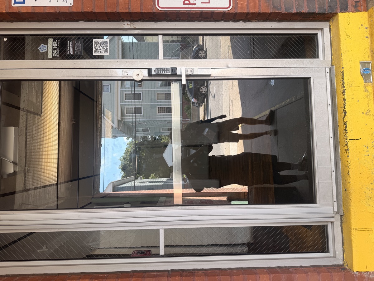Close-up of the studio's glass entrance door with keypad entry and a 24-hour surveillance sticker.